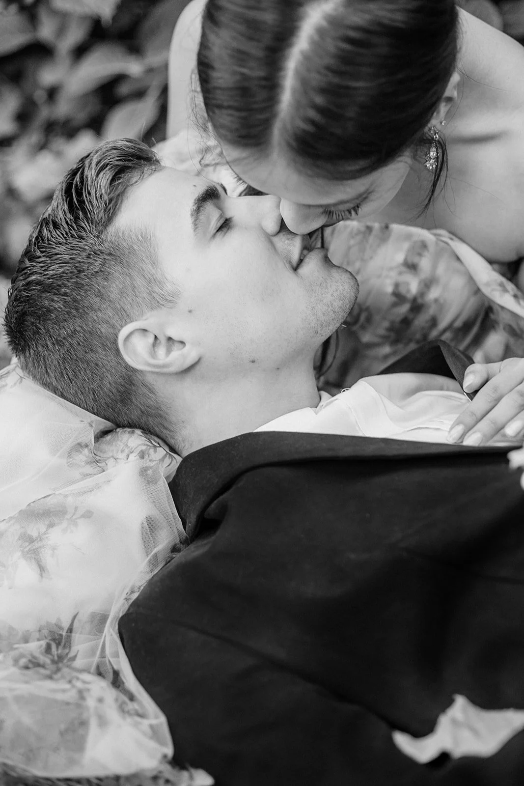 Black-and-white close-up of couple kissing while lying down, groom in suit and bride in floral dress