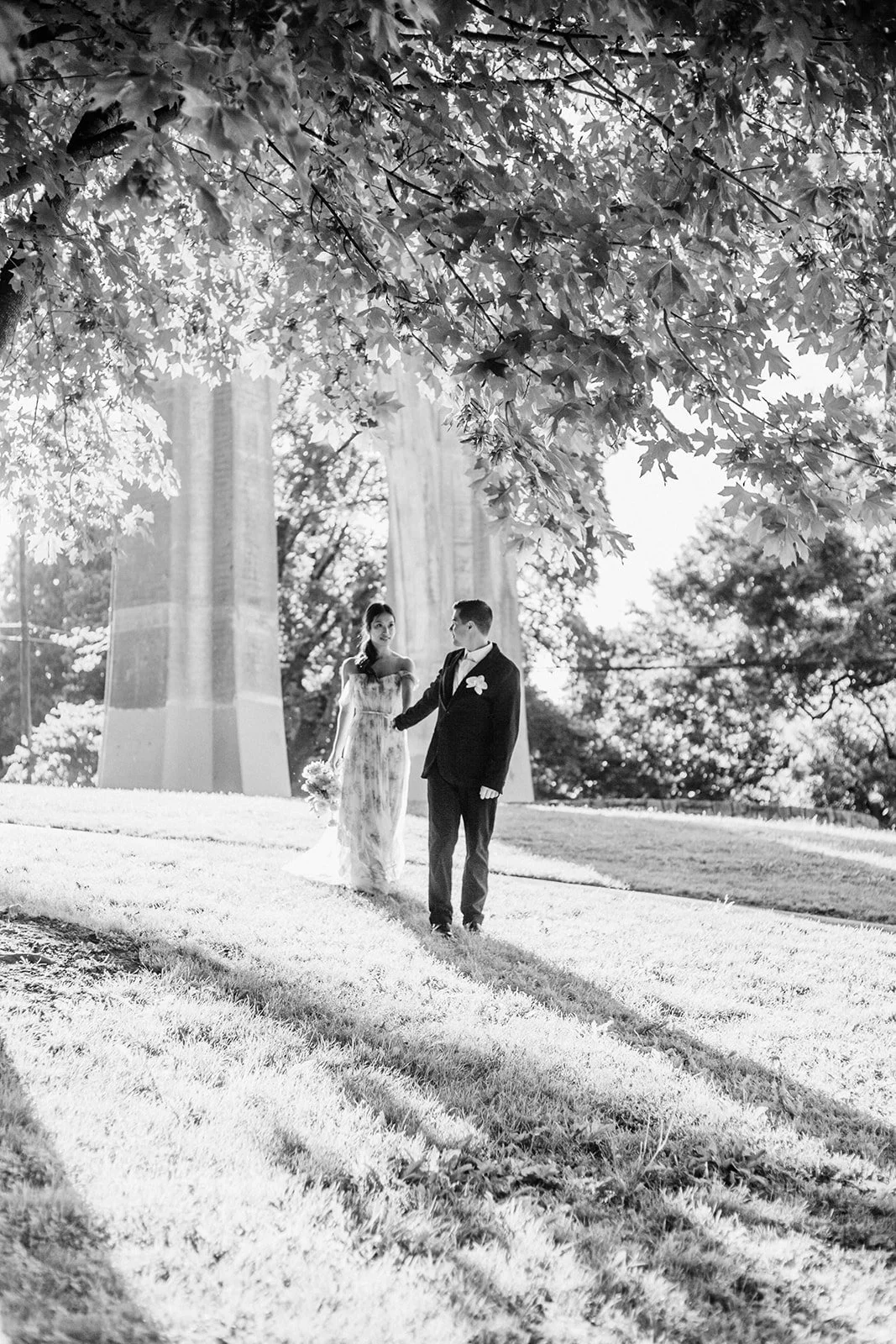 Black-and-white photo of couple holding hands and walking outdoors, bride carrying bouquet