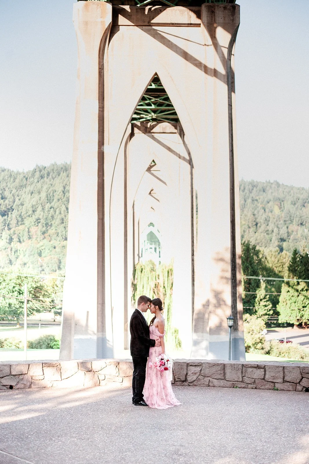 Couple standing beneath tall Cathedral Park bridge arches, framed by architecture.