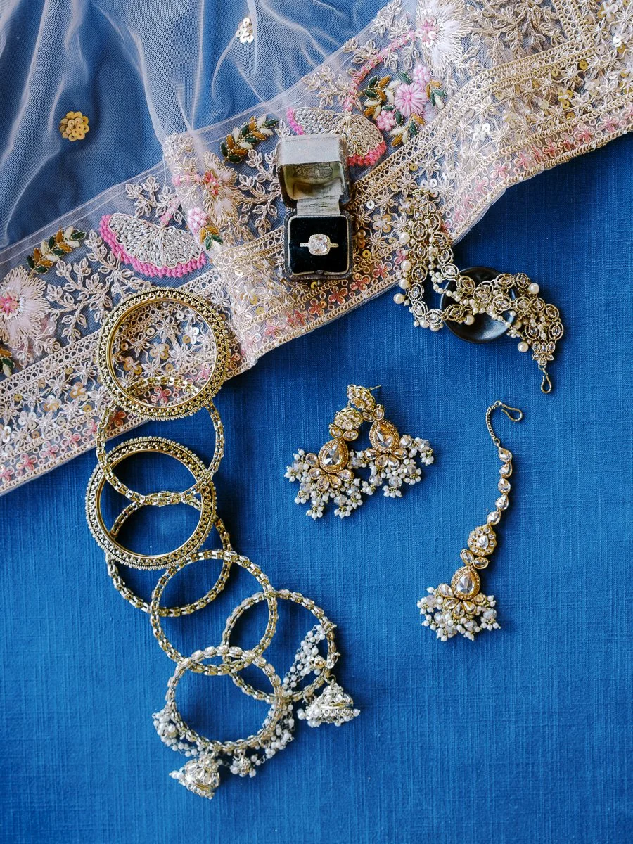 Bridal dupatta, gold bangles, earrings, and engagement ring styled flat lay for a luxury South Asian wedding detail photo.