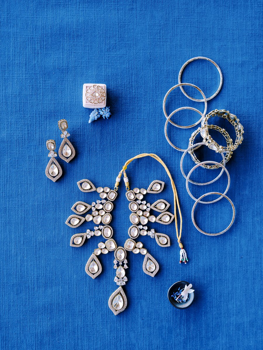 Modern South Asian bridal jewelry set with earrings, bangles, and statement necklace styled on textured royal blue fabric.