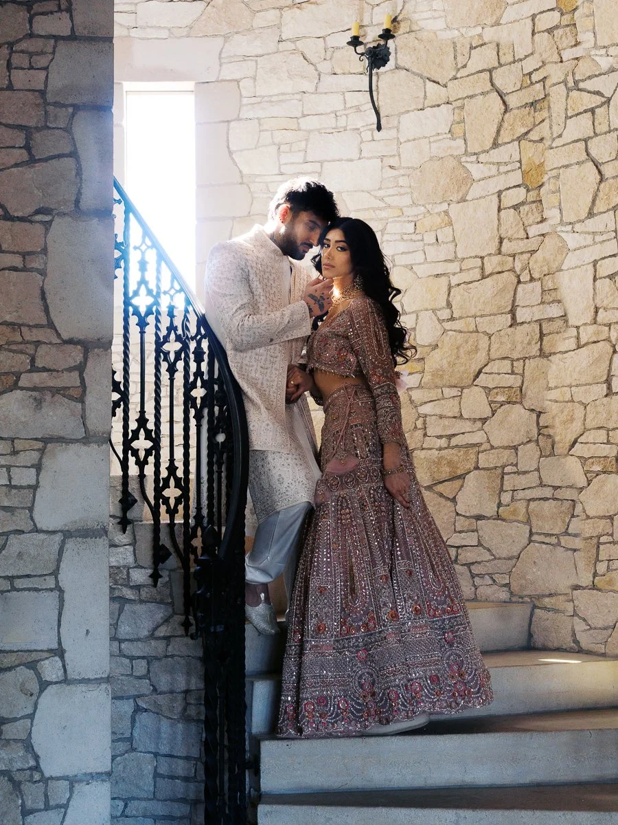 Elegant South Asian couple portrait on curved stone staircase wearing pastel lehenga and ivory sherwani at Chateau de Lis.