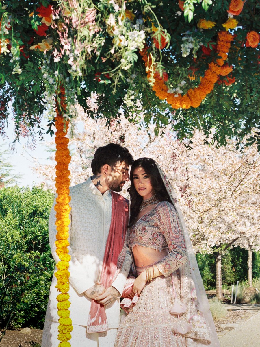 Romantic South Asian wedding portrait beneath hanging florals and marigold garlands during outdoor spring ceremony.