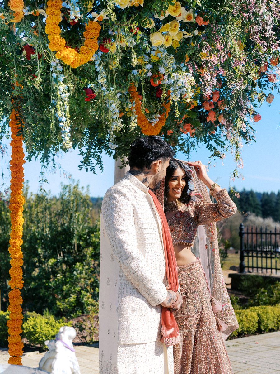 South Asian bride and groom standing beneath hanging florals and marigold garlands during outdoor wedding ceremony at Chateau de Lis.