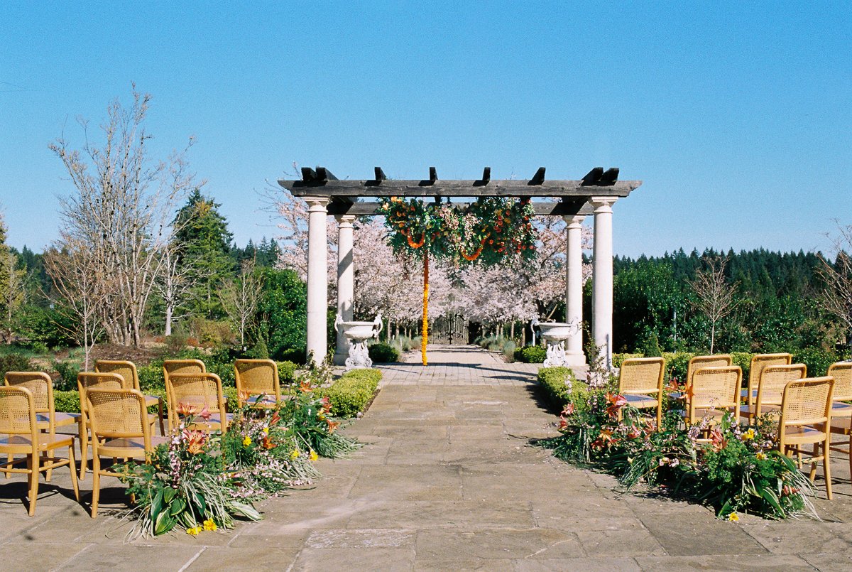 Outdoor wedding ceremony aisle with floral arrangements and pergola setup at Chateau de Lis under clear spring skies.