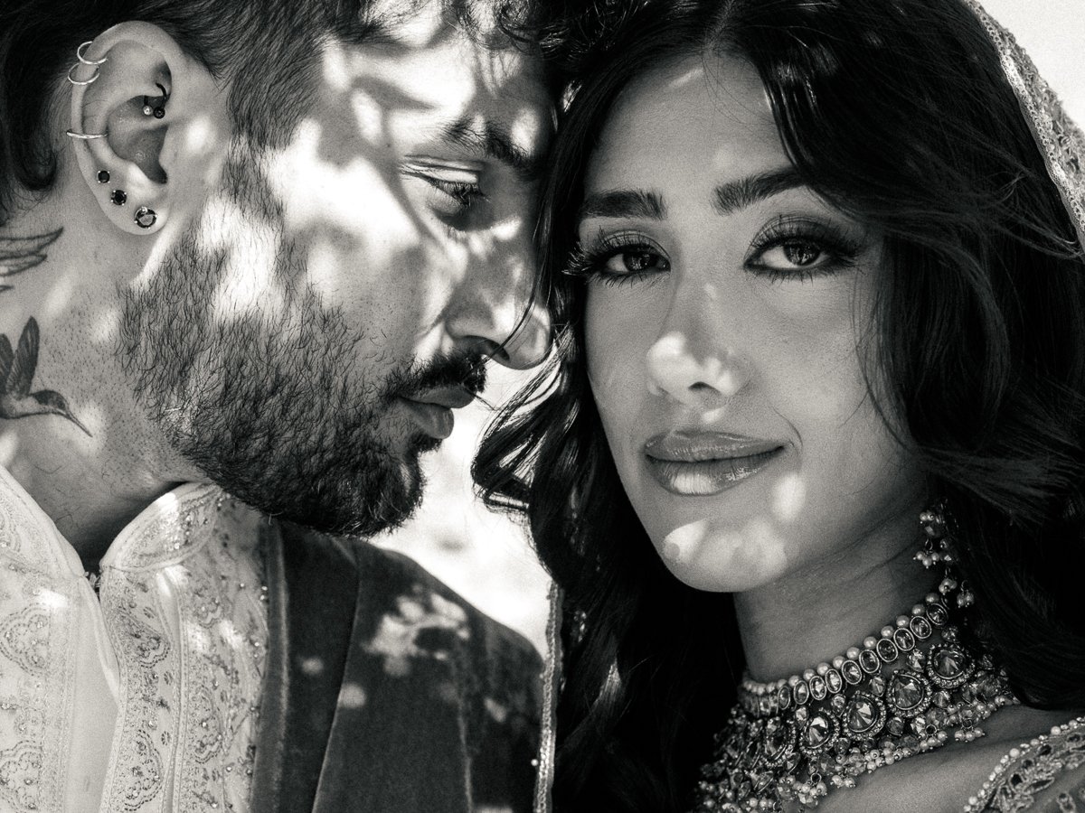 Black and white portrait of South Asian bride and groom beneath dappled floral shadows in an intimate outdoor moment.