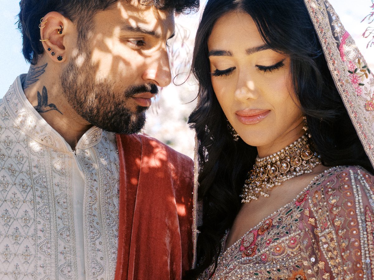 Close-up portrait of South Asian couple in embroidered wedding attire with soft sunlight and detailed bridal jewelry.