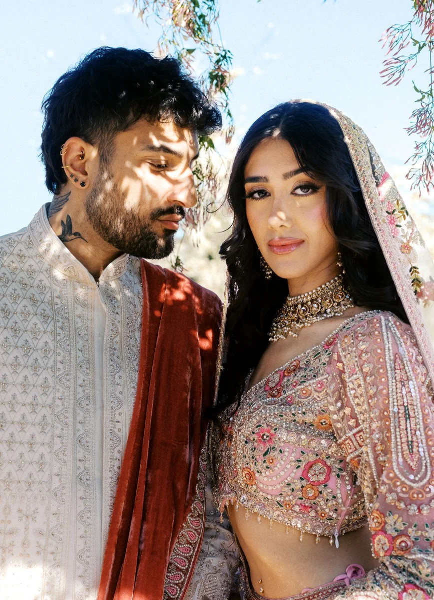 Elegant South Asian couple portrait with pastel lehenga, ivory sherwani, and floral veil details at spring wedding celebration.