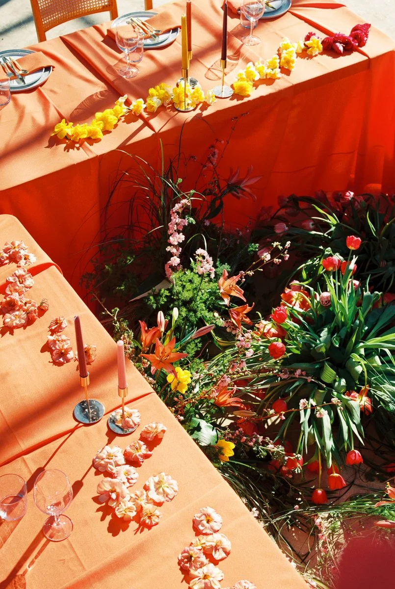 Overhead view of colorful floral reception installation with tulips, lilies, and spring blooms beneath vibrant orange tables.