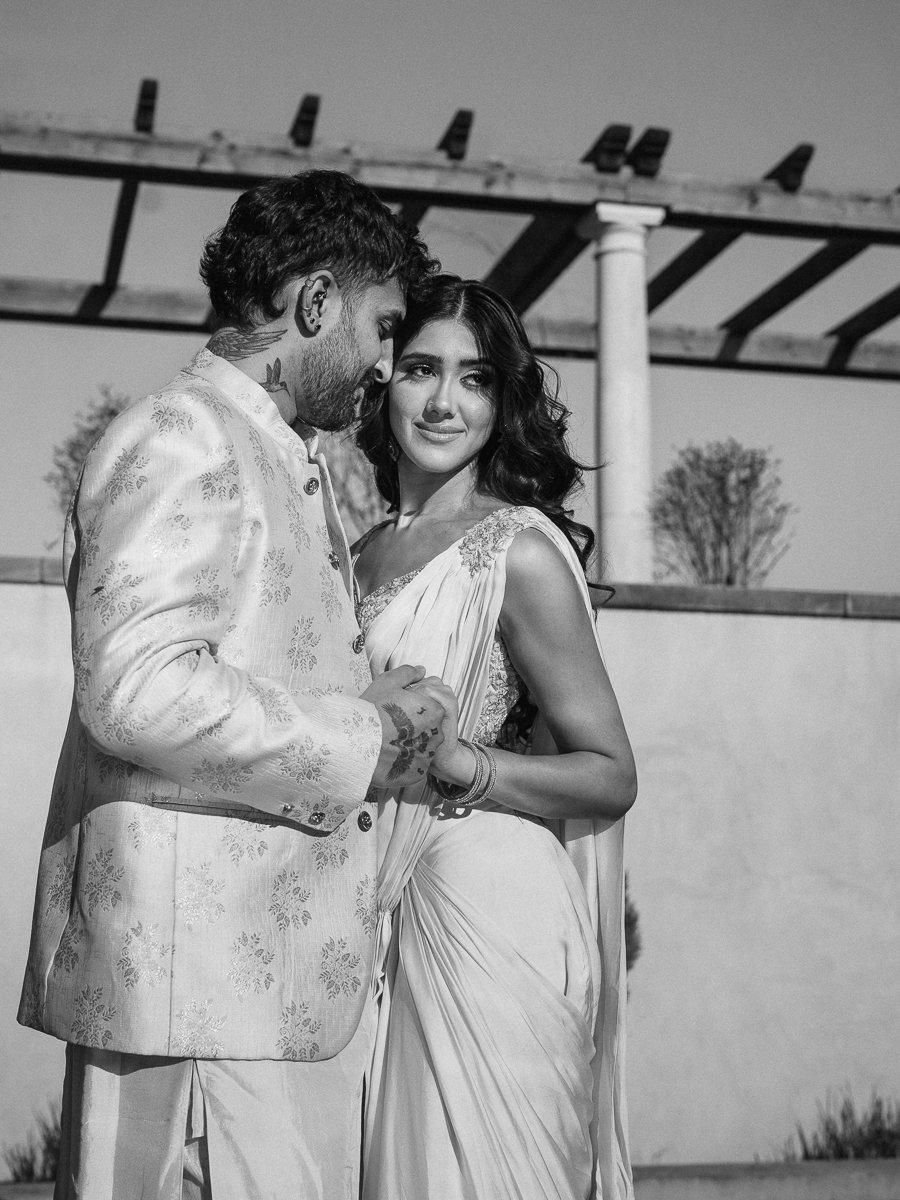 Black-and-white portrait of couple embracing outdoors in coordinated pastel South Asian formalwear.