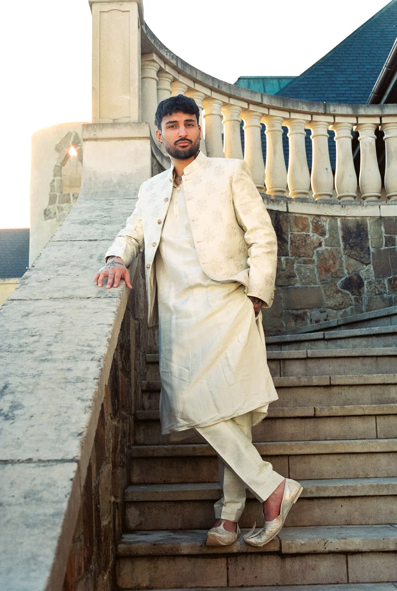 Groom portrait on stone staircase wearing ivory sherwani and embroidered loafers during wedding session.