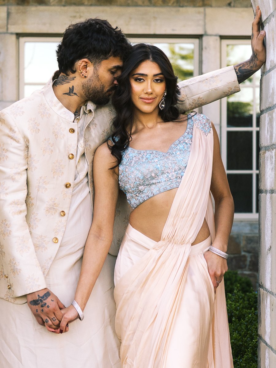 Close-up portrait of South Asian couple embracing beside stone wall in pastel formalwear.