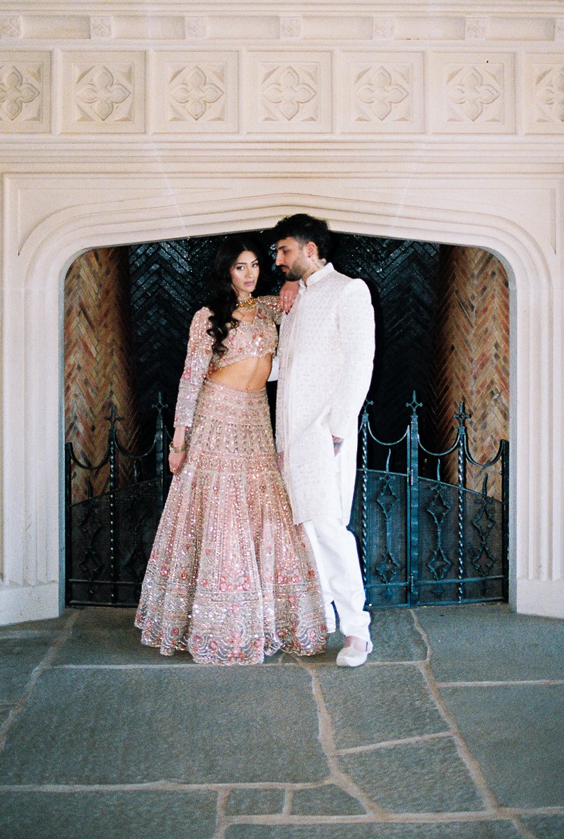 Couple in ornate Indian wedding attire posing beneath an arched fireplace at Chateau de Lis in Oregon.