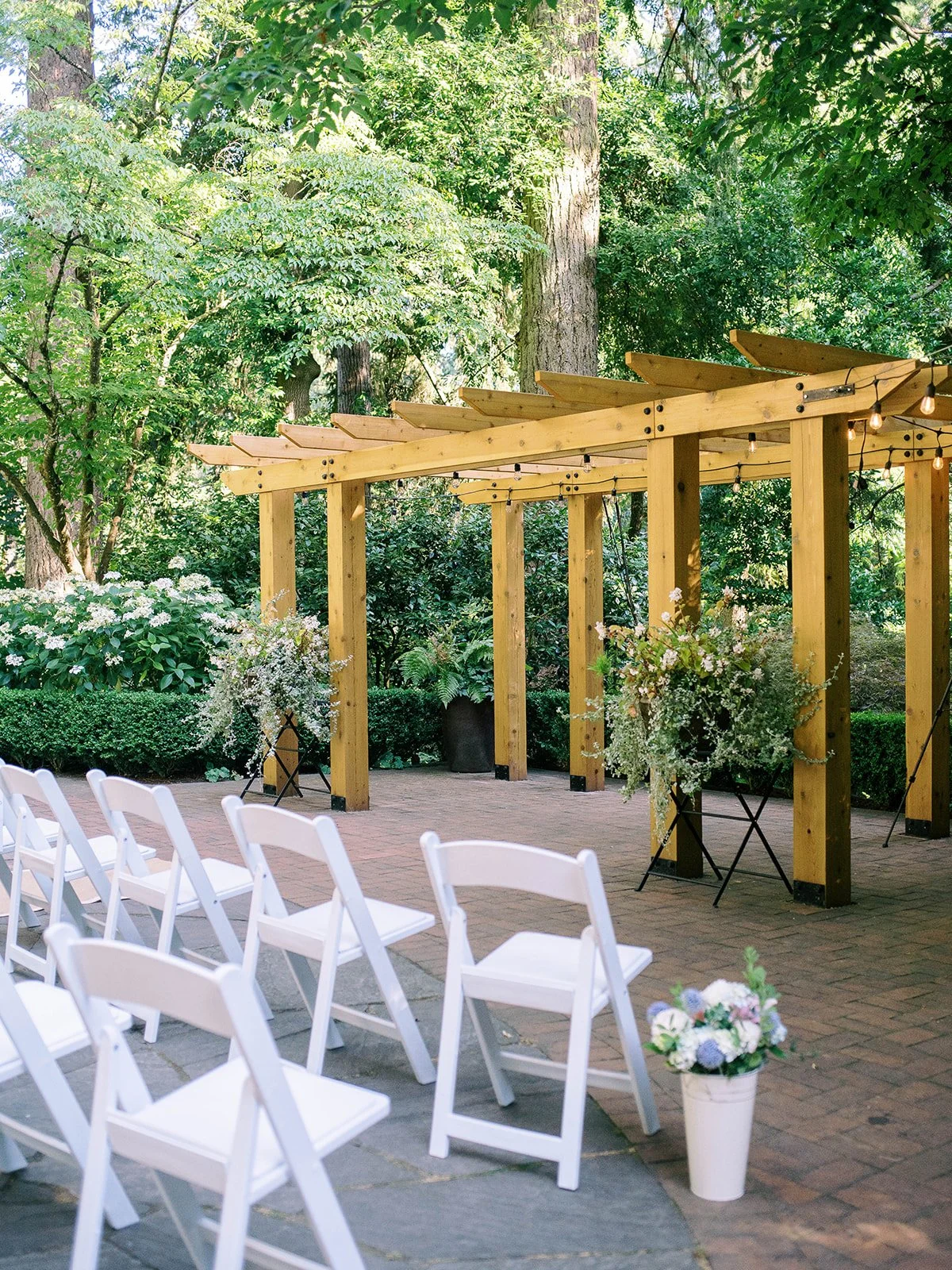 Outdoor wedding ceremony setup with white chairs and a wooden pergola at Leach Botanical Garden.