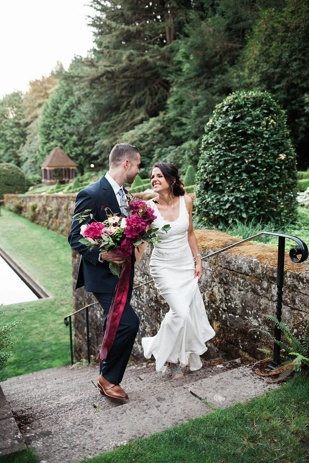 Bride and groom walking through landscaped gardens at Lewis &amp; Clark College wedding venue.