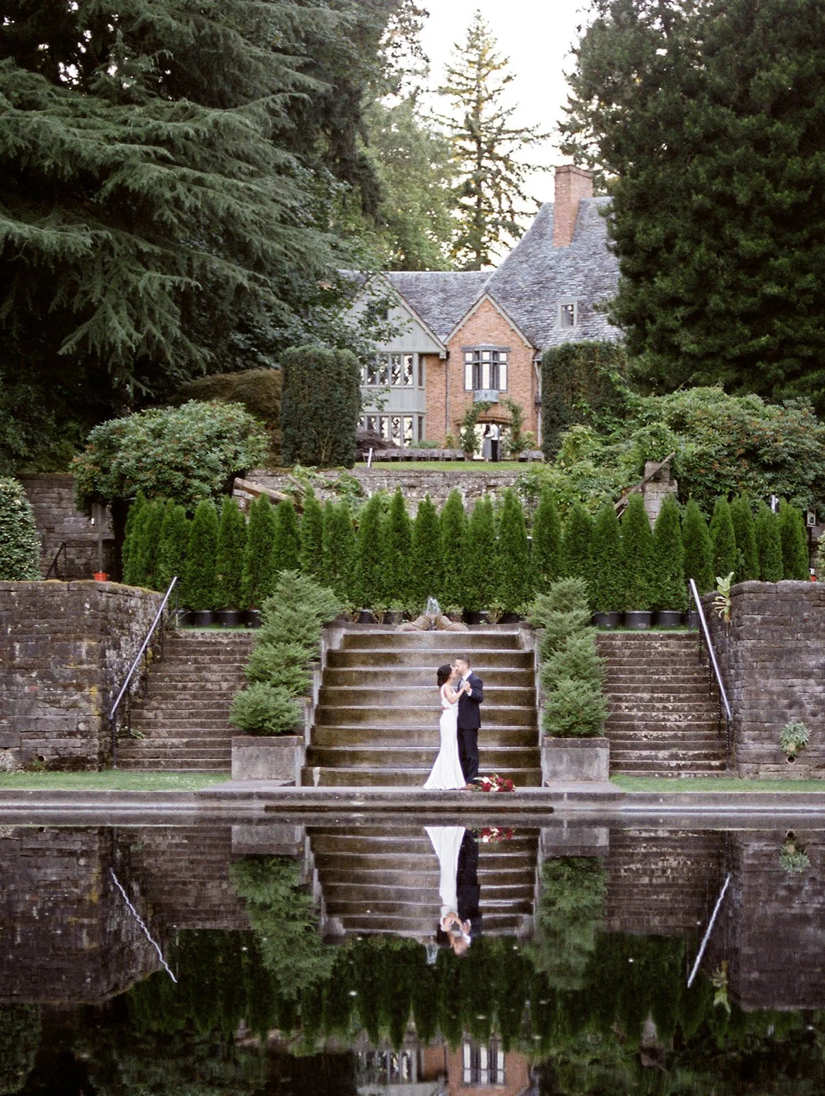 Wedding couple standing on stone steps beside a reflecting pool at Lewis &amp; Clark College in Portland.