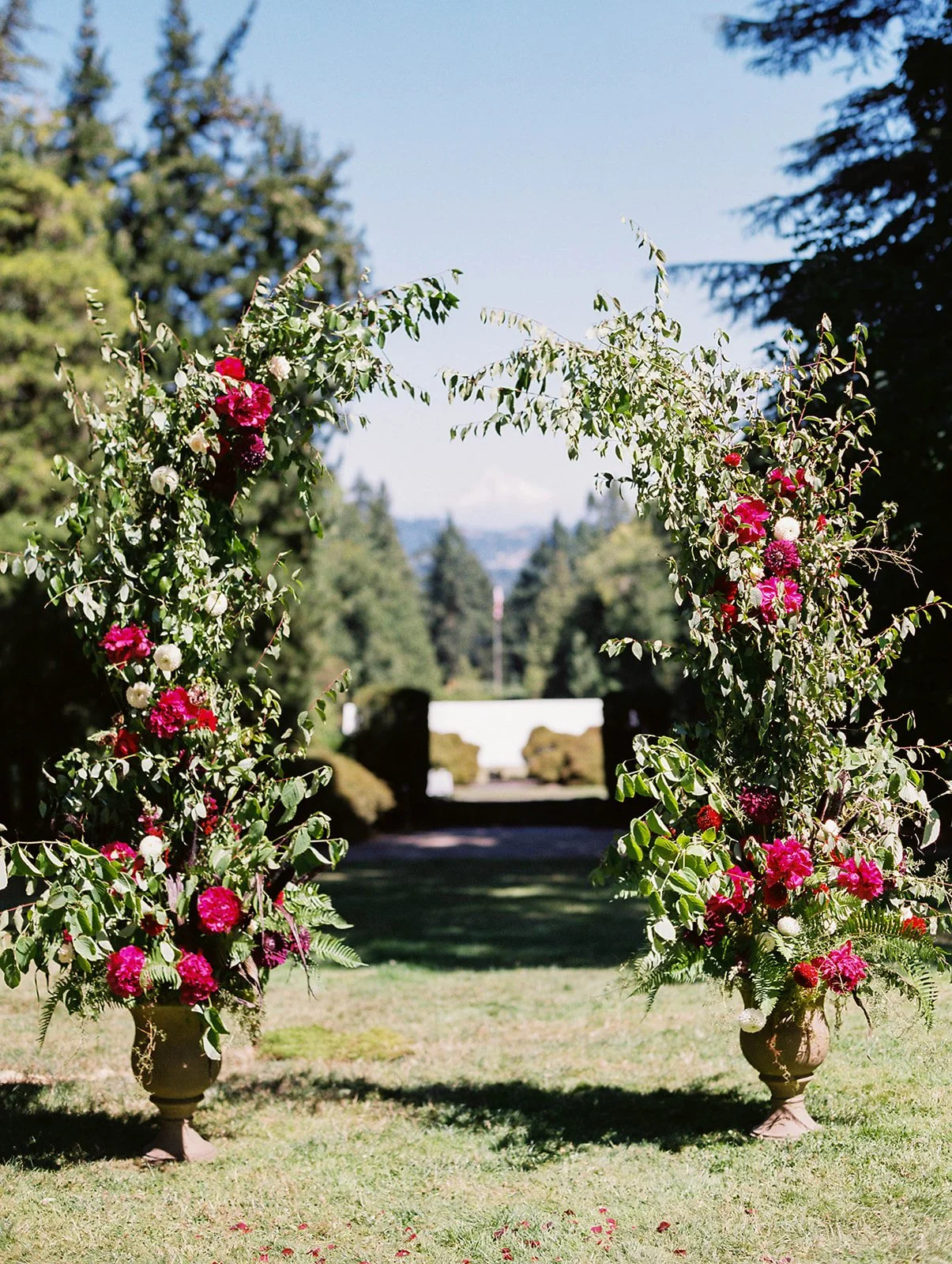 Greenery and deep pink flowers forming an outdoor wedding ceremony arch at Lewis &amp; Clark College.