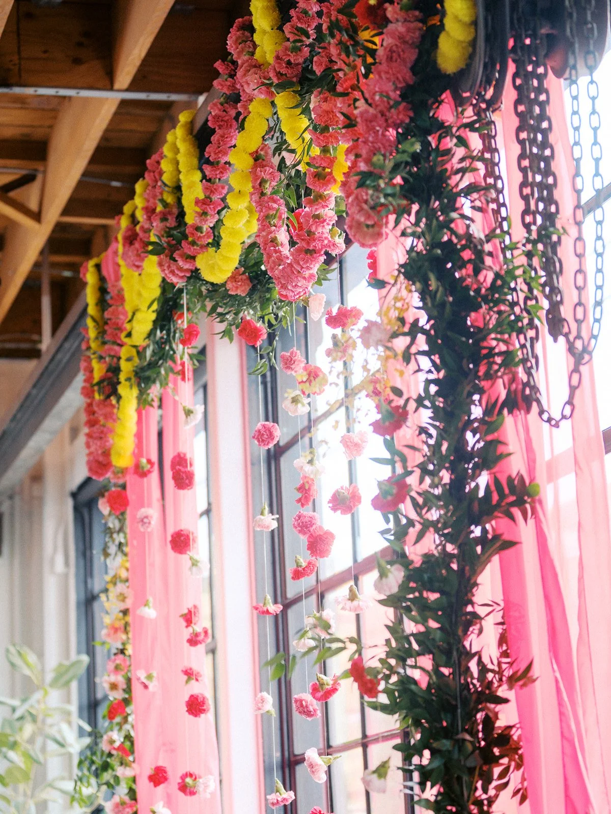 Pink and yellow floral garlands hanging beside industrial windows at Castaway Portland wedding venue.