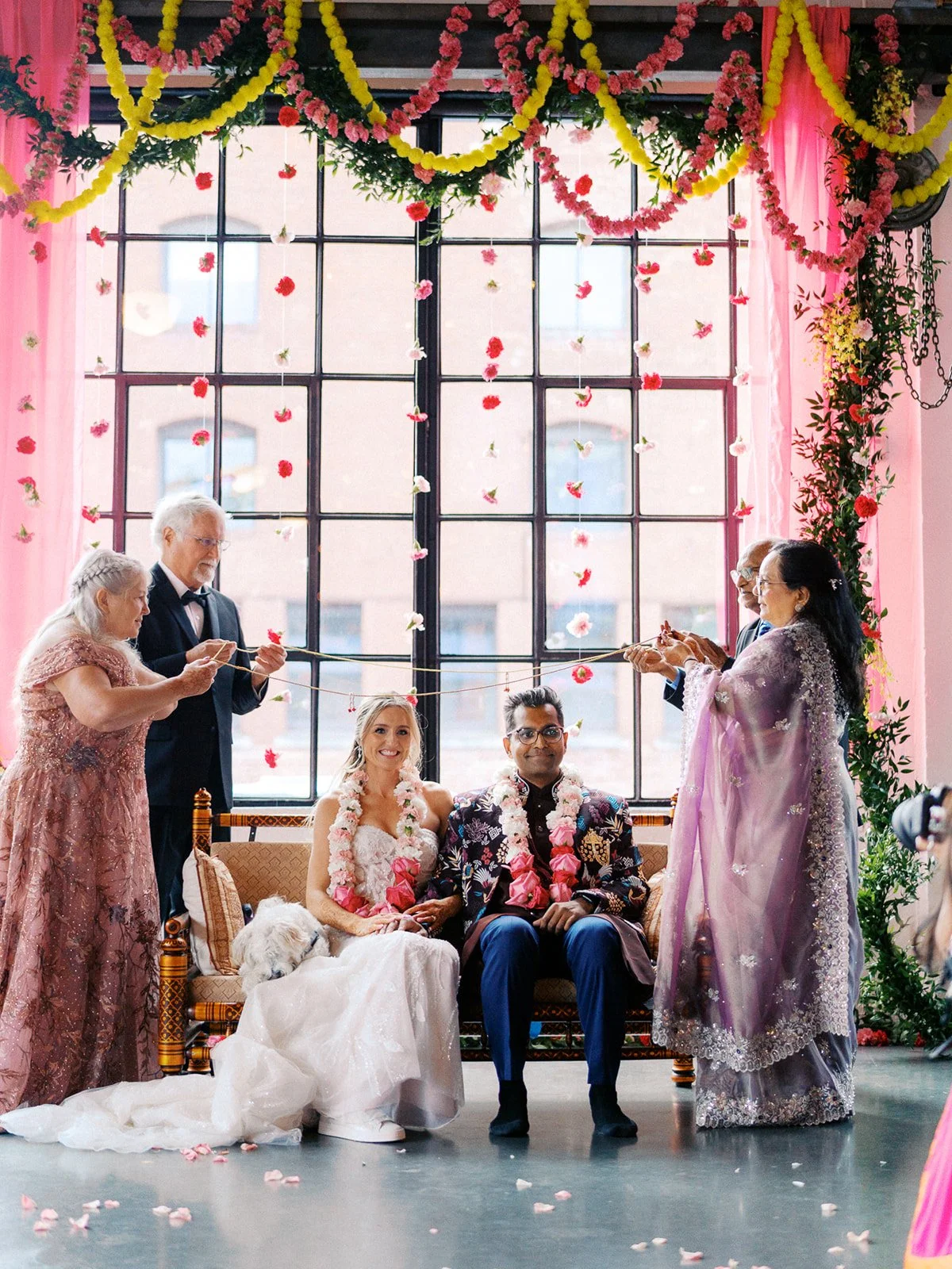 Wedding couple seated beneath colorful floral garlands during a ceremony at Castaway Portland in Oregon.