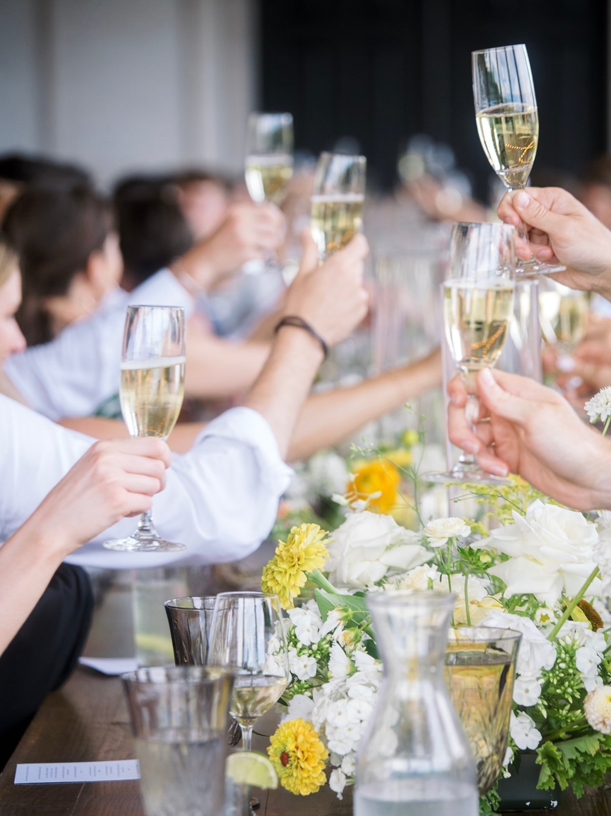 Wedding guests raise champagne glasses for a toast beside white and yellow floral centerpieces in Oregon.