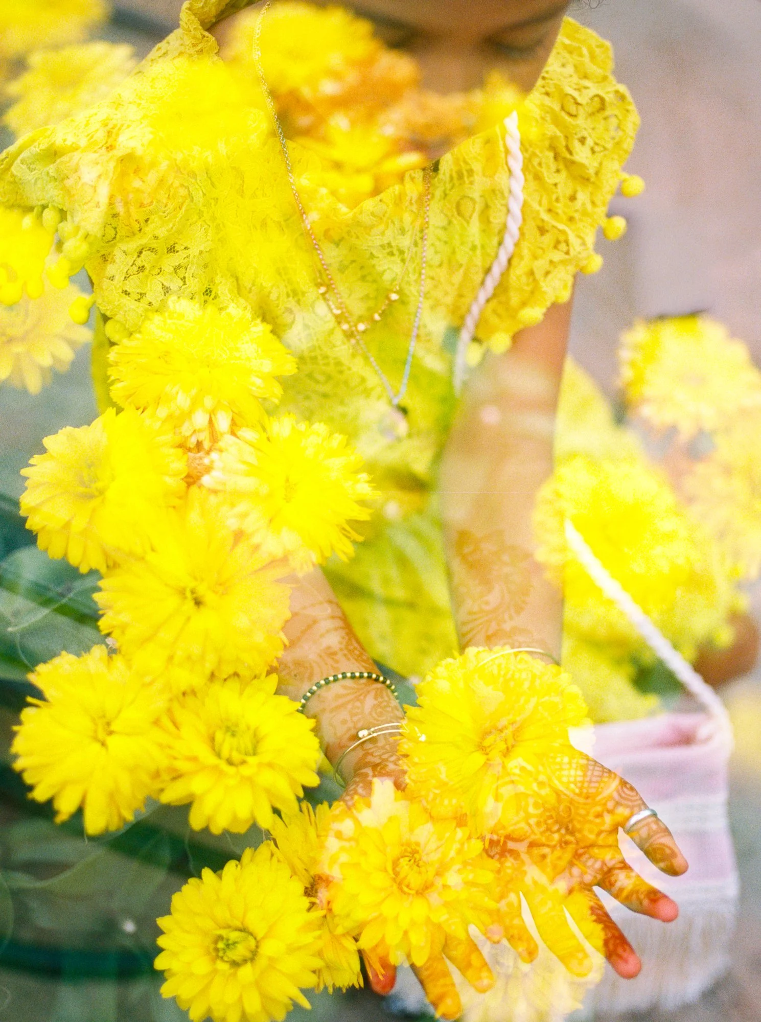 Close-up of henna-covered hands surrounded by bright yellow flowers during the Haldi ceremony.