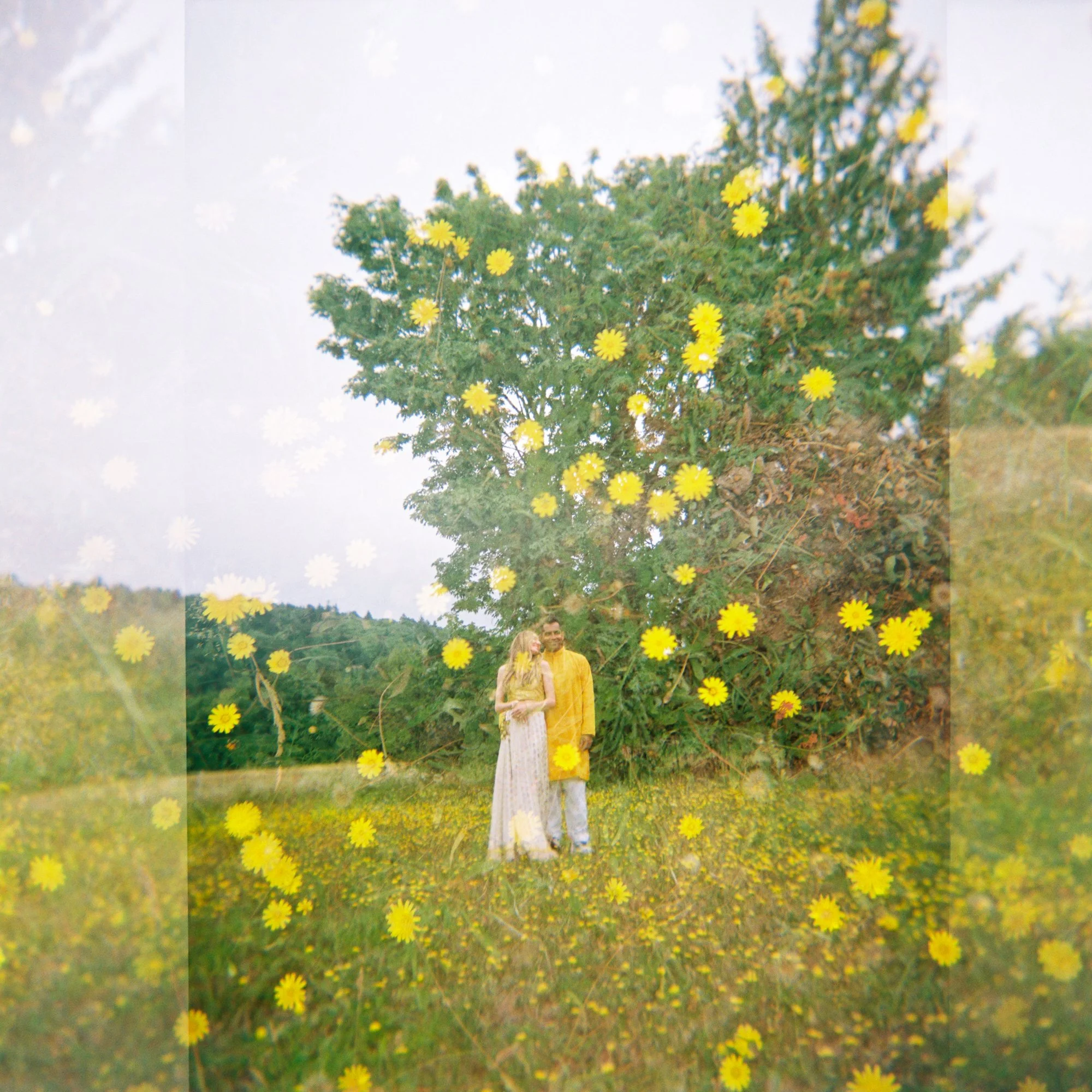 Double-exposure portrait of Alacia and Rohit standing in a meadow filled with yellow wildflowers.