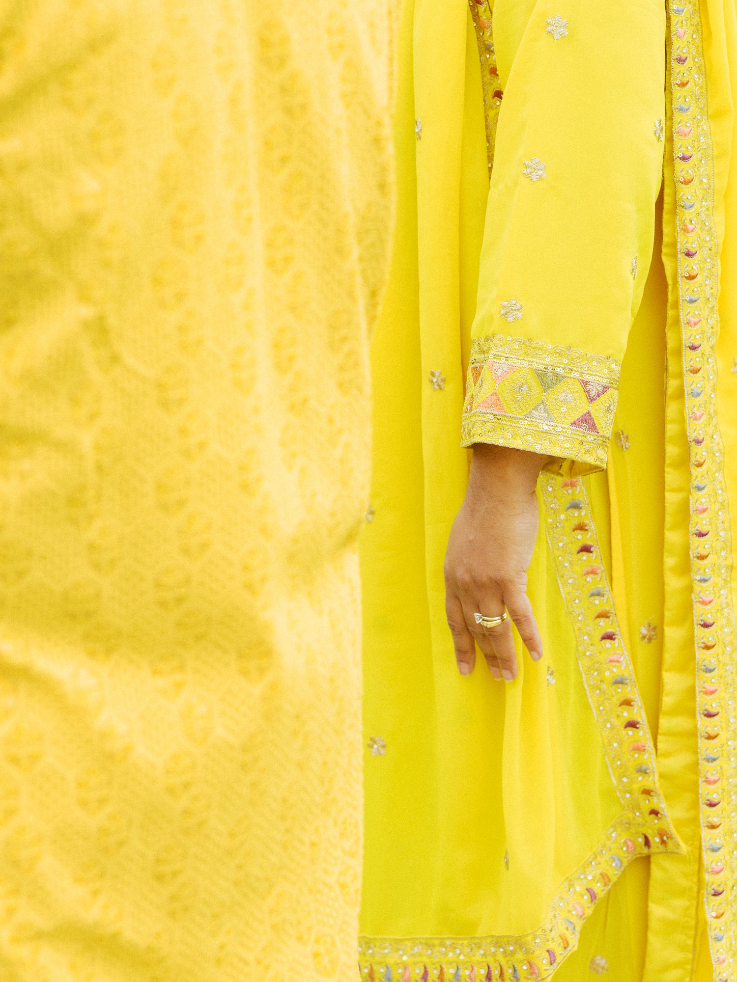 Detail of a bright yellow embroidered outfit worn for the Haldi celebration.