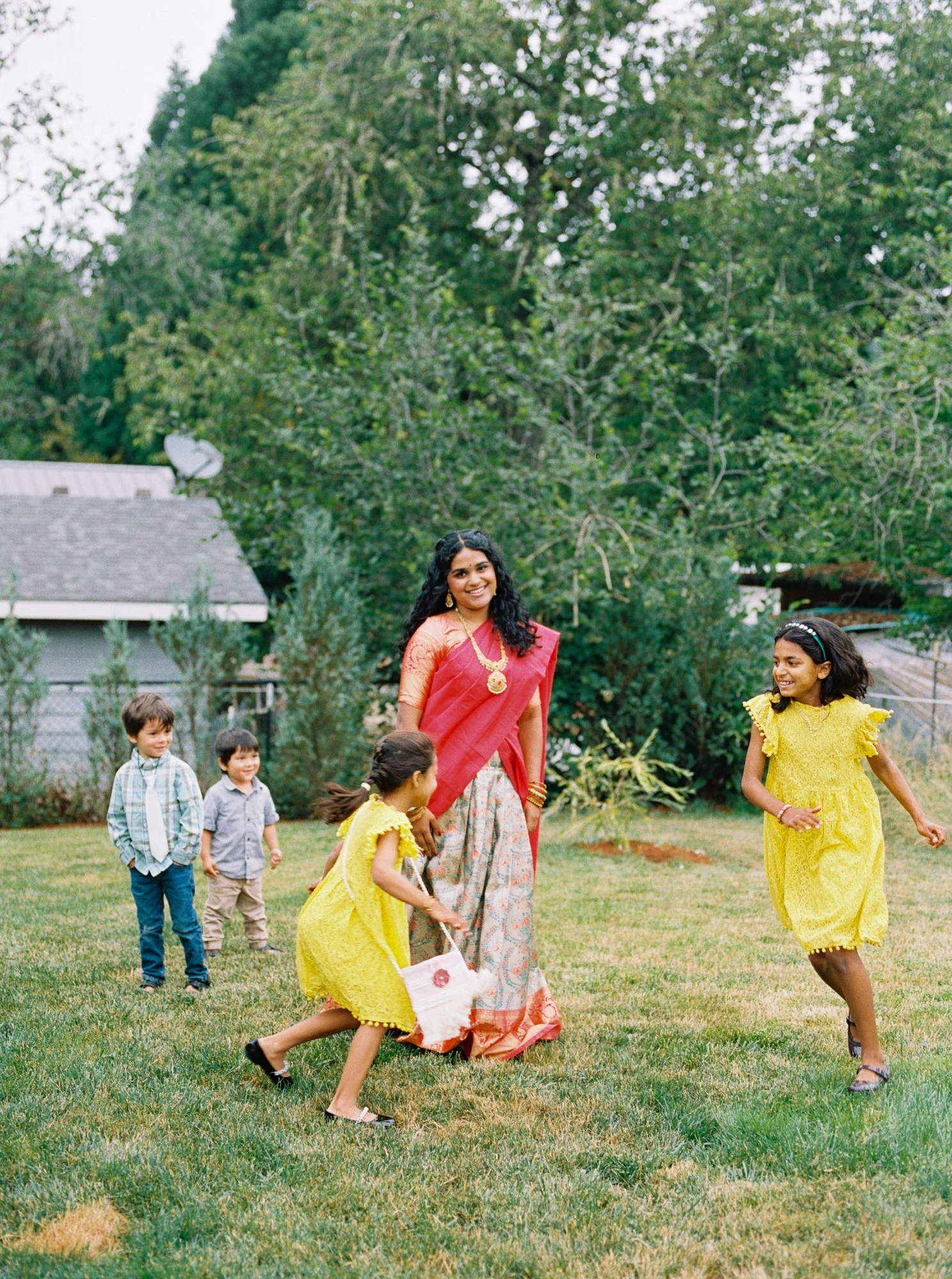 Children and guests in colorful traditional clothing gather on the lawn during the Haldi celebration.