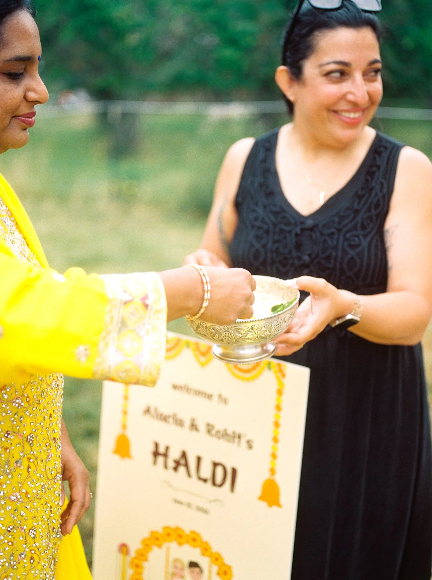 Guests pass a decorative bowl during the Haldi ceremony with the welcome sign visible behind them.