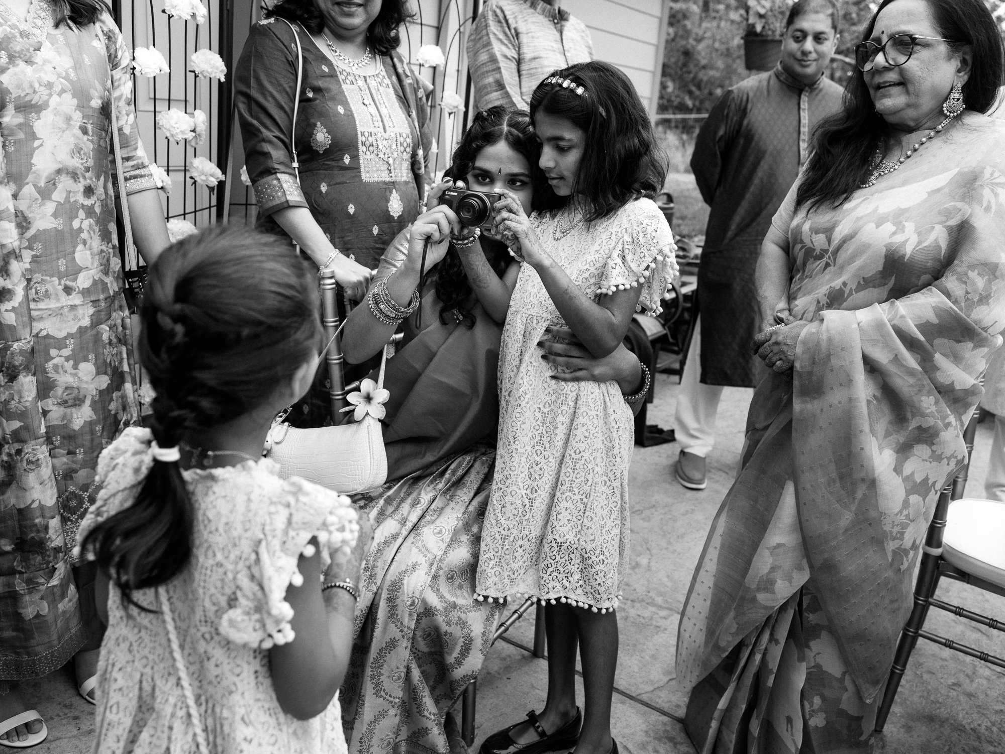 Guests gather as a child looks through a camera during an outdoor Haldi celebration.