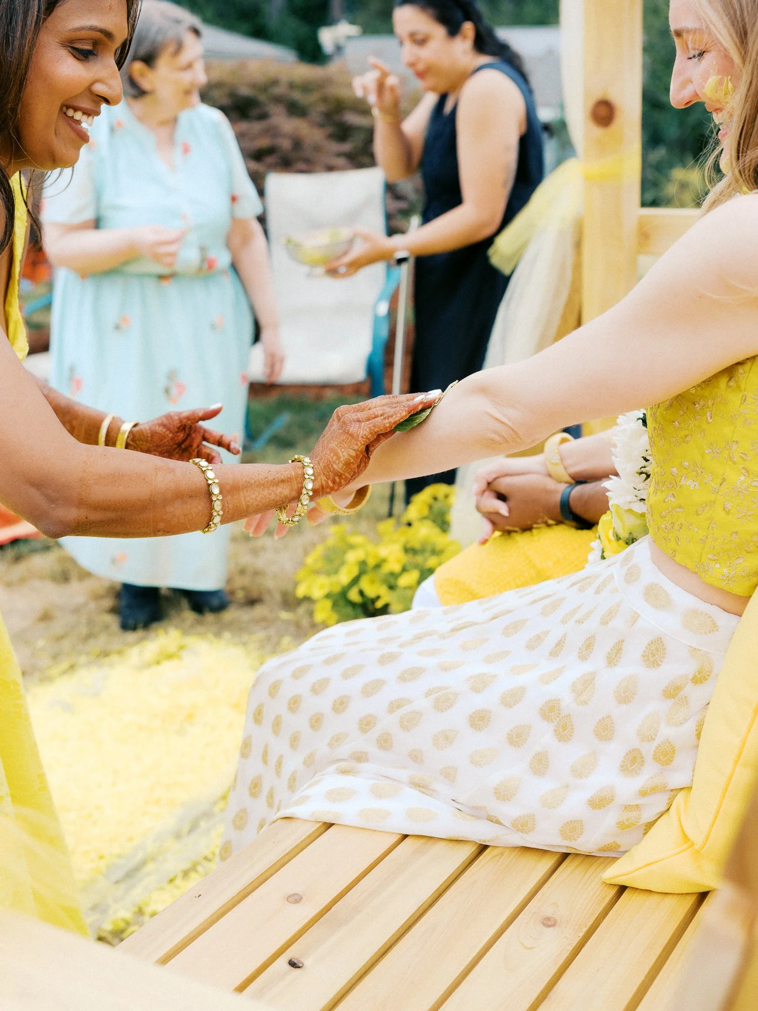 Guest with henna-covered hands applies turmeric paste to the bride’s arm during the Haldi ceremony.