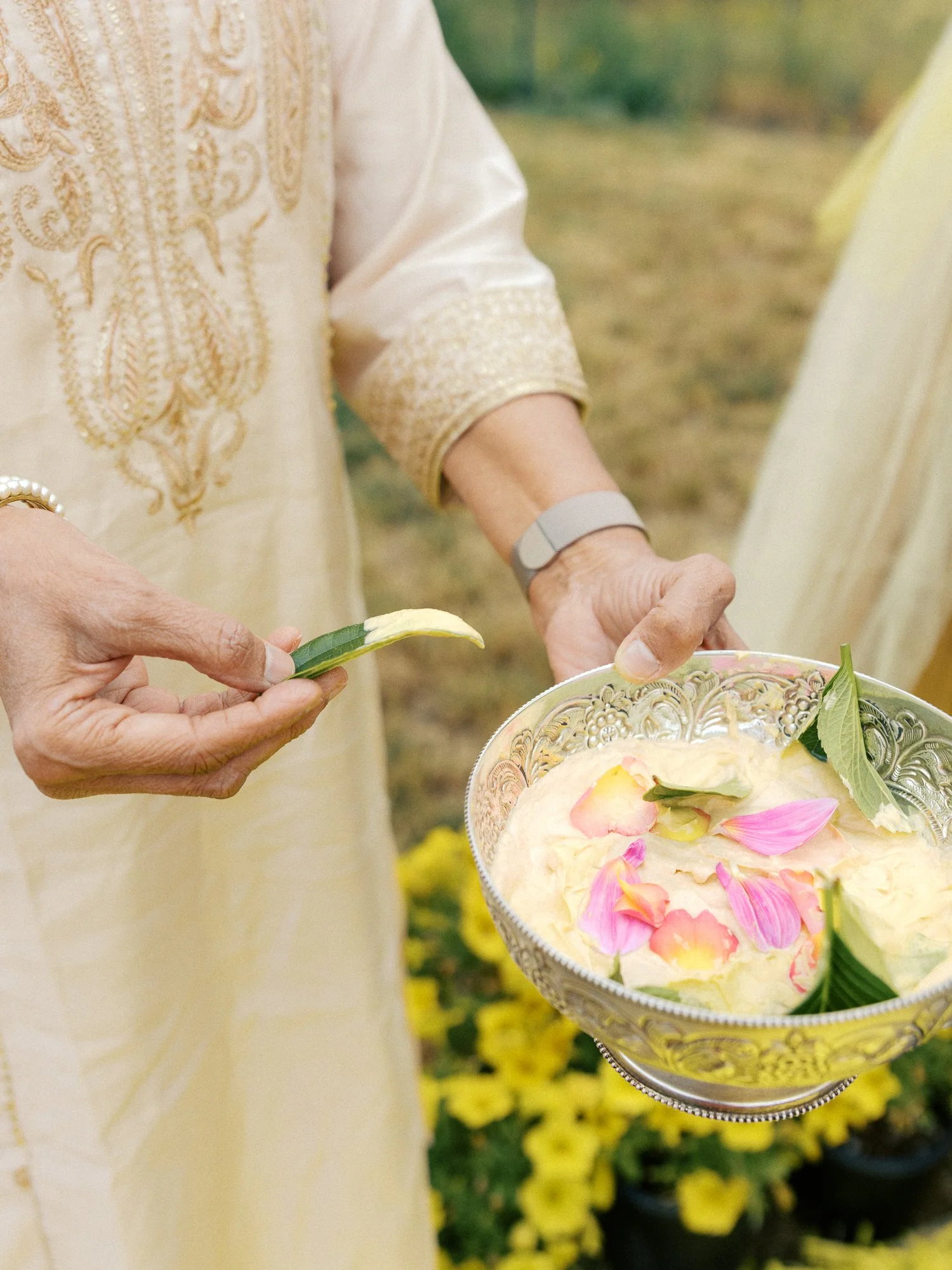 Close-up of turmeric paste with flower petals and leaves in an ornate silver bowl during the Haldi ceremony.