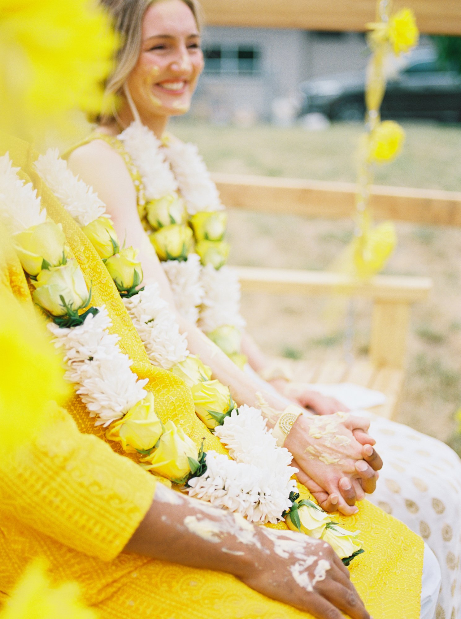 Close-up of the couple holding hands with flower garlands and turmeric paste during Haldi.