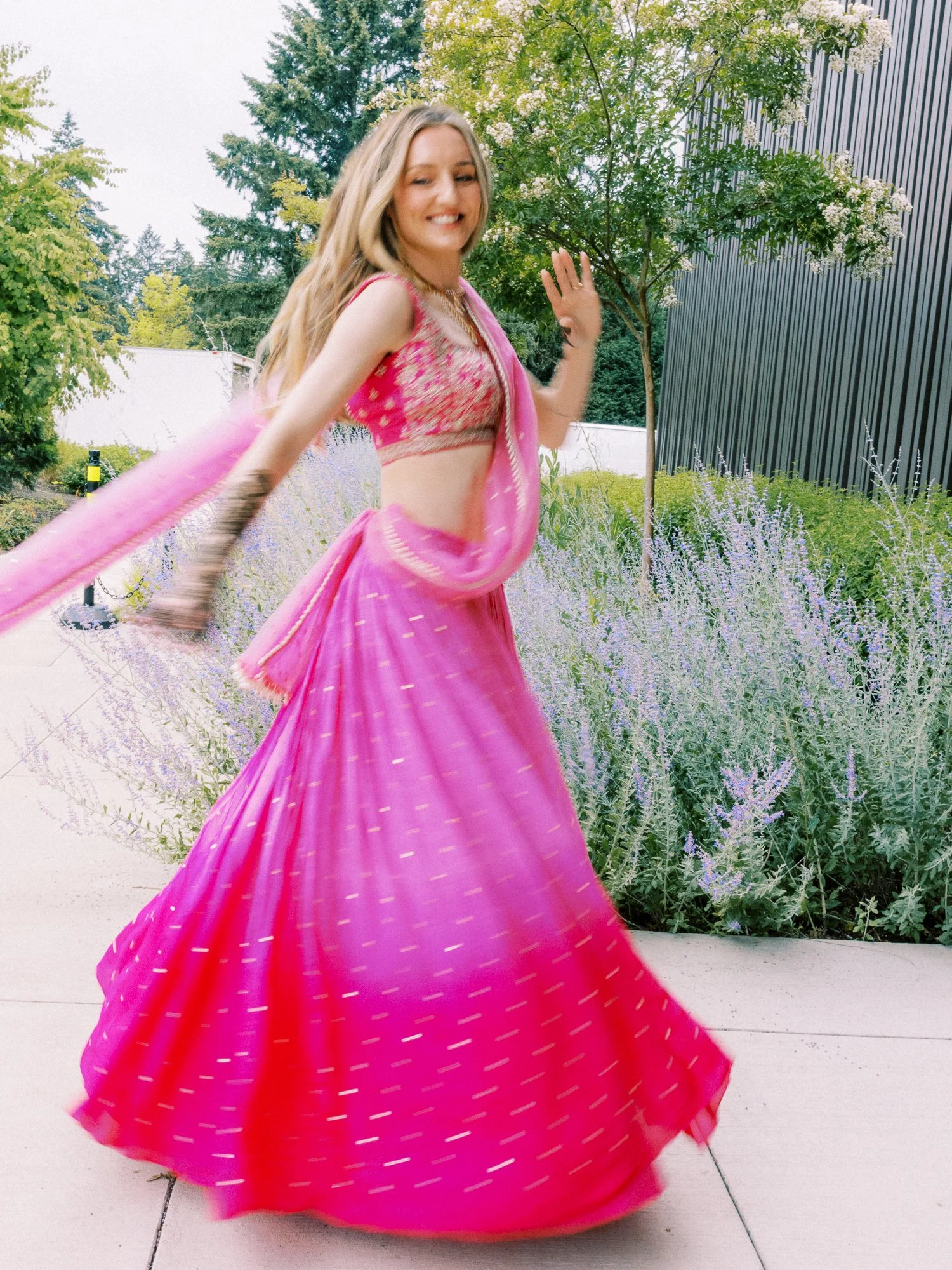 Alacia twirling outdoors in a bright pink lehenga during the Mehndi celebration.