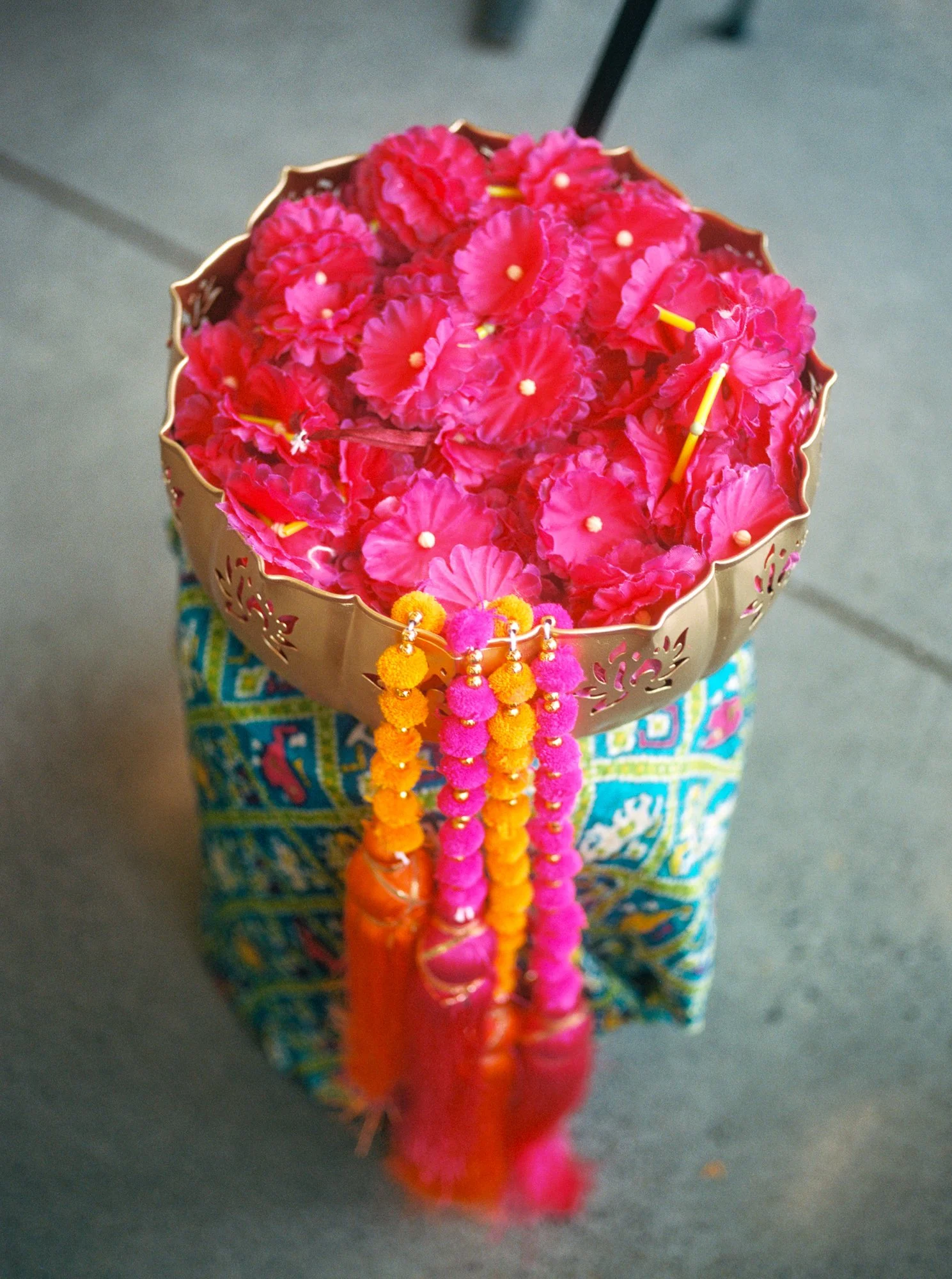 Gold decorative bowl filled with bright pink flowers and colorful tassels for the Mehndi celebration.