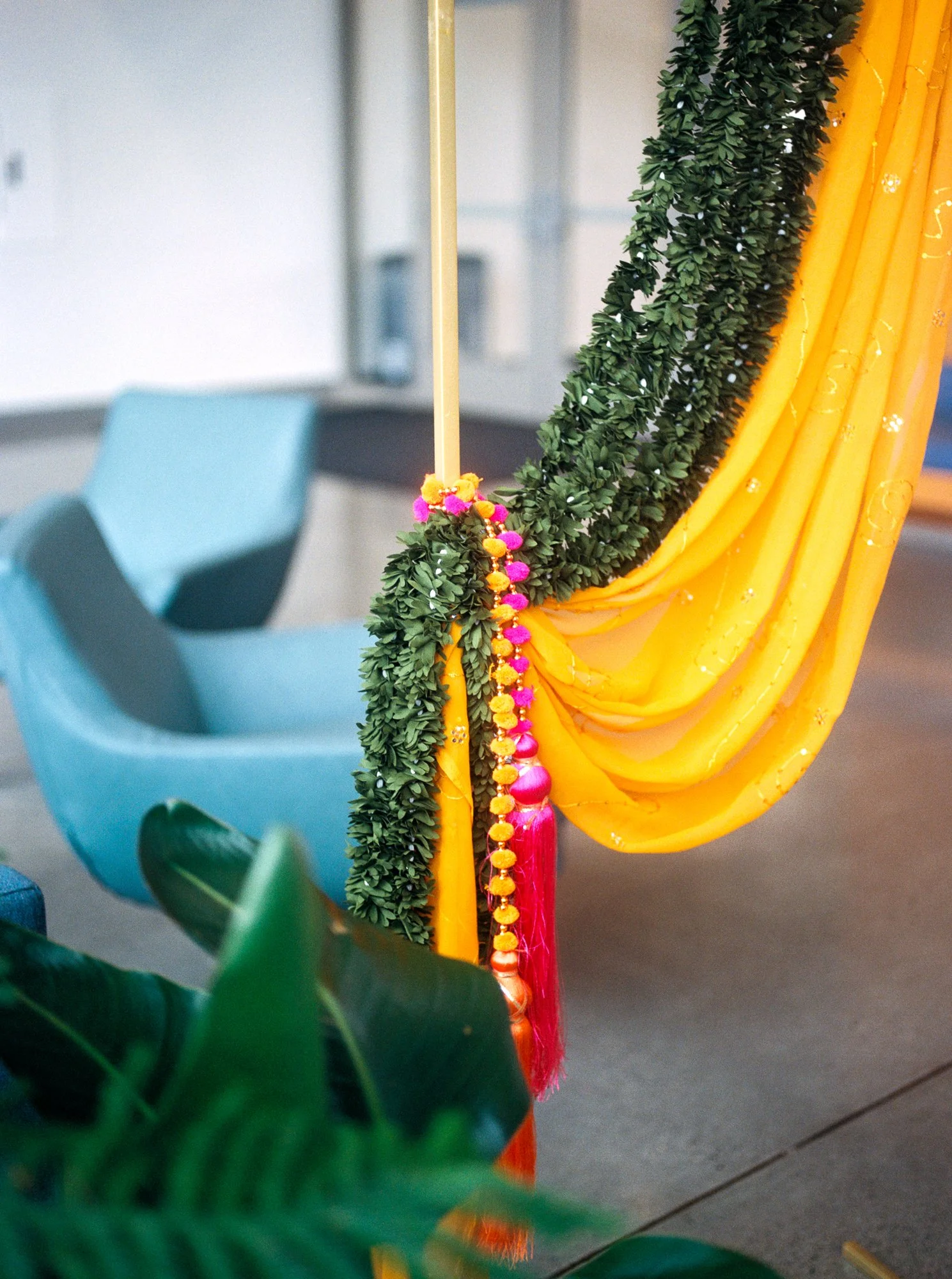 Close-up of yellow fabric, greenery, and pink-orange tassels decorating the Mehndi ceremony entrance.