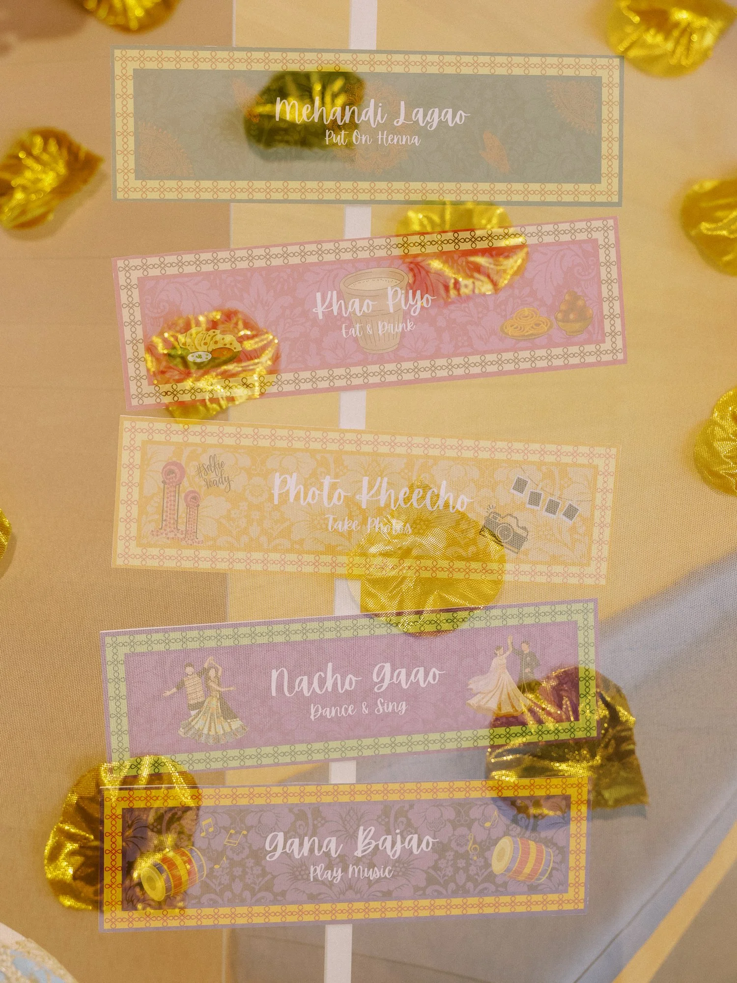 Mehndi activity sign listing henna, food, photos, dancing, and music beneath gold floral decorations.