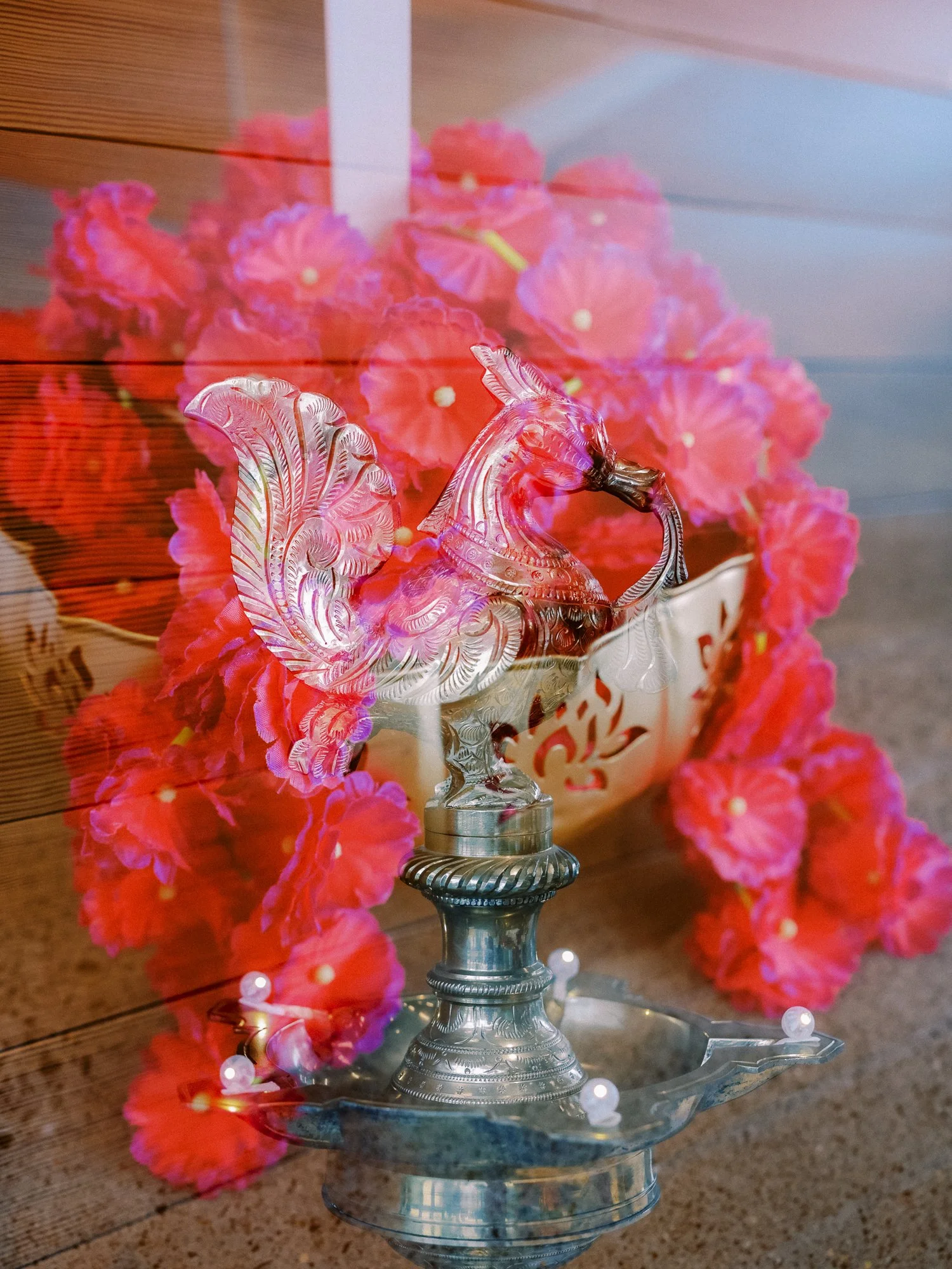 Decorative silver peacock lamp surrounded by vivid pink flowers at the Mehndi celebration.