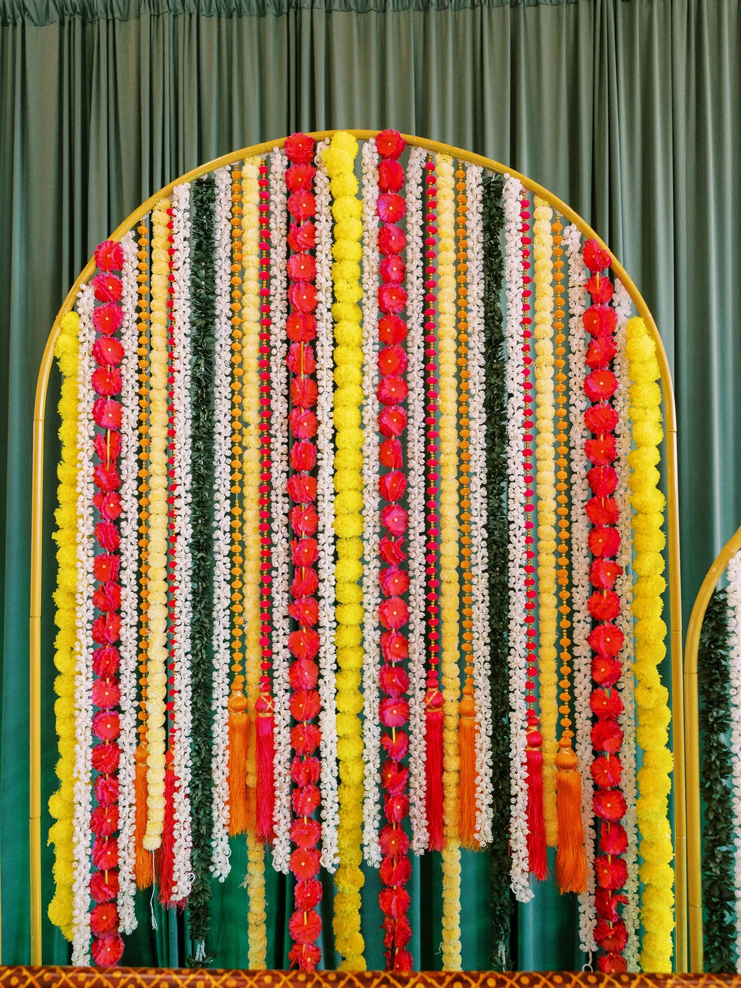 Colorful Mehndi backdrop covered in hanging red, yellow, white, and green floral garlands.