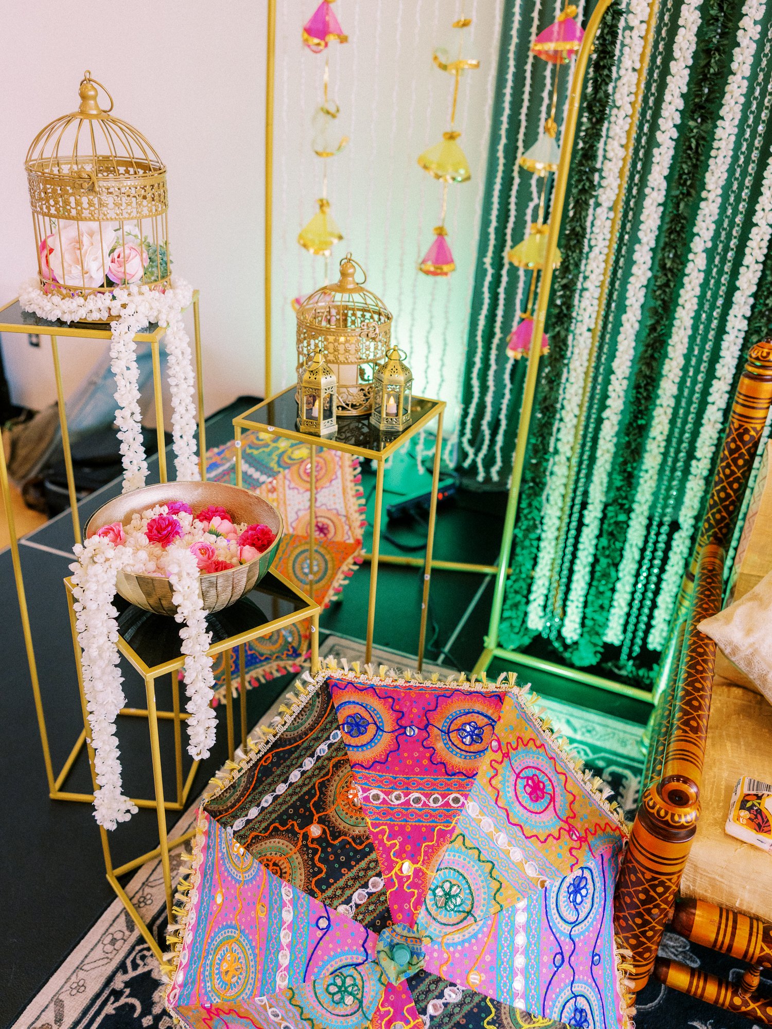 Mehndi decor with gold lanterns, white flower garlands, colorful textiles, and a patterned umbrella.