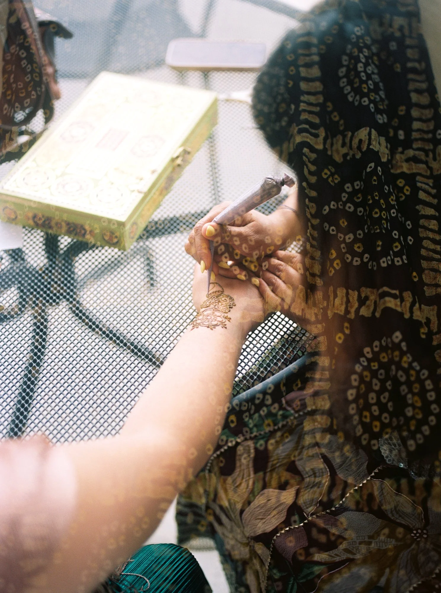 Henna artist applying an intricate floral design to a guest’s forearm during the Mehndi ceremony.