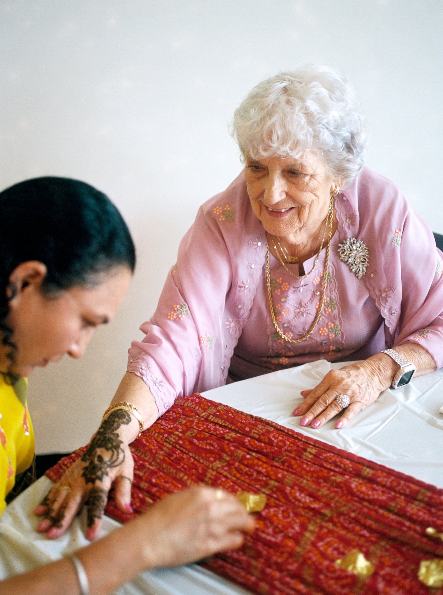 Older guest in a pink traditional outfit receiving henna on her hand during the Mehndi celebration.