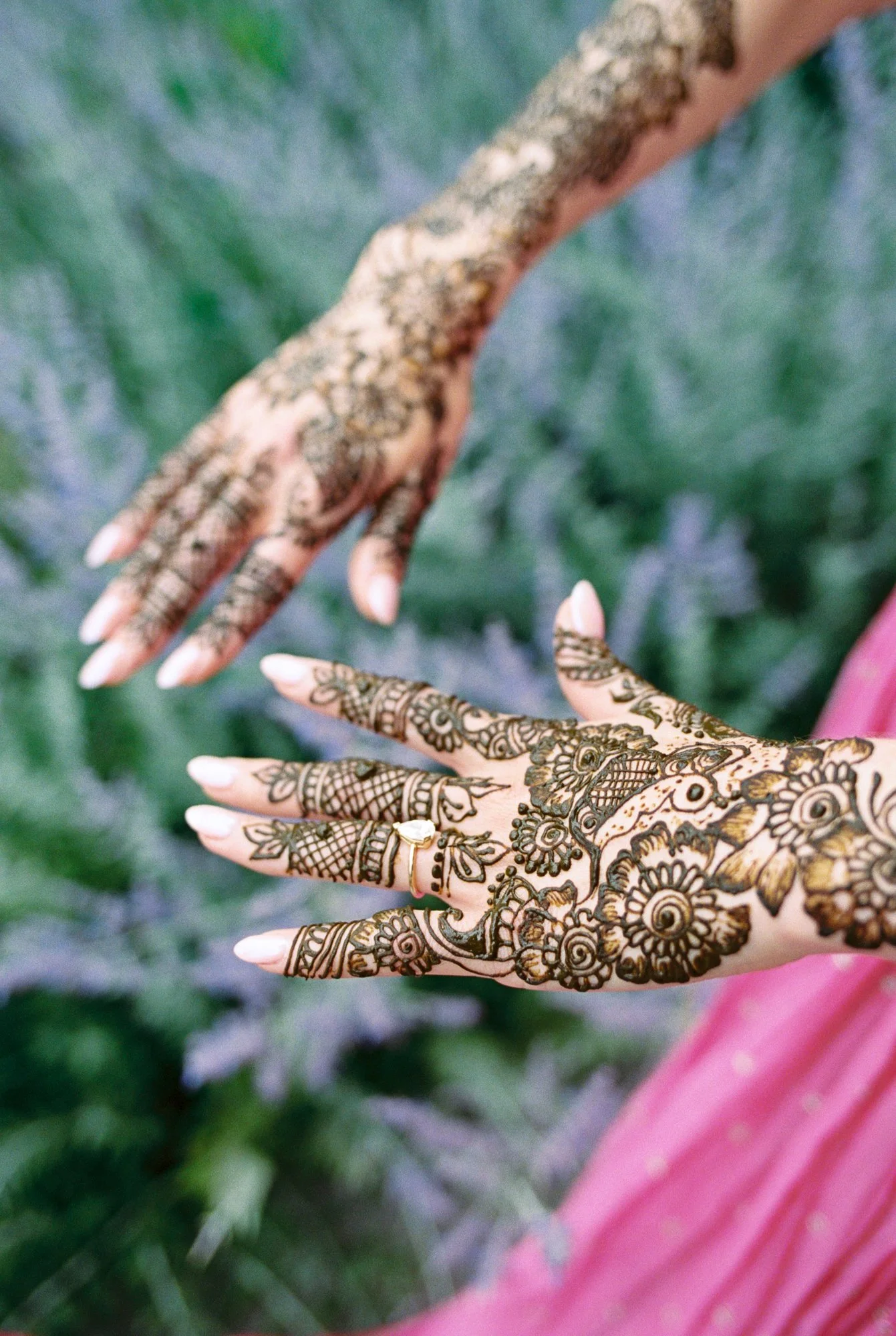 Close-up of intricate floral Mehndi designs covering both hands against a bright pink outfit.