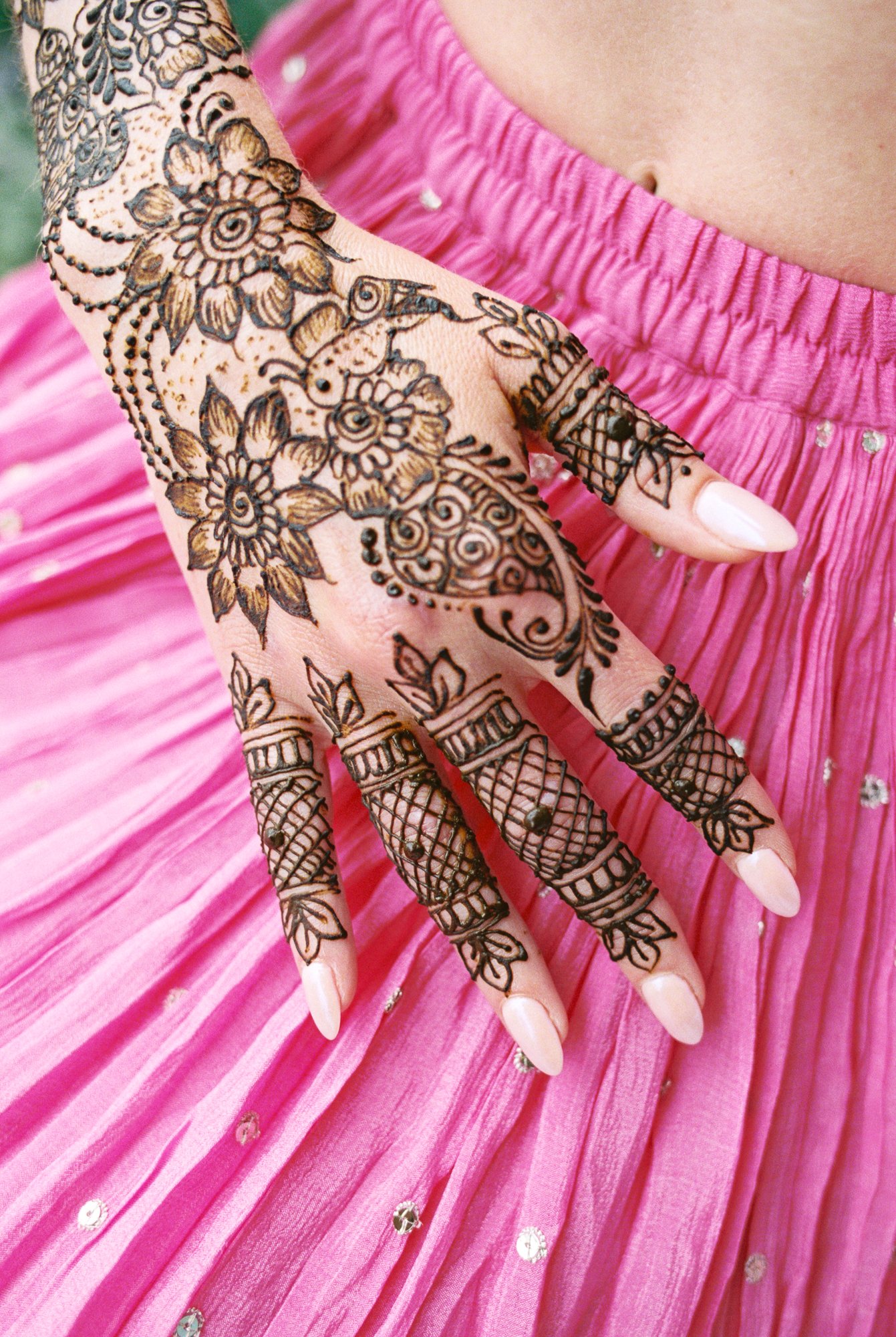 Detailed henna pattern with flowers and paisley covering Alacia’s hand against her pink skirt.