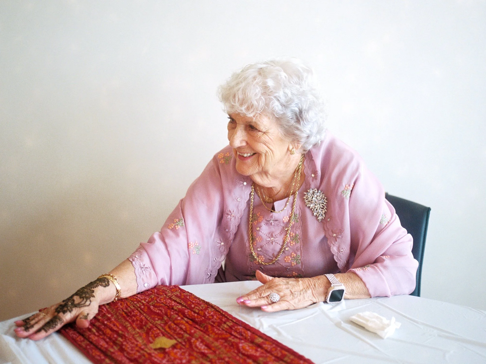 Older guest smiling while showing fresh henna on her hand at the Mehndi ceremony.