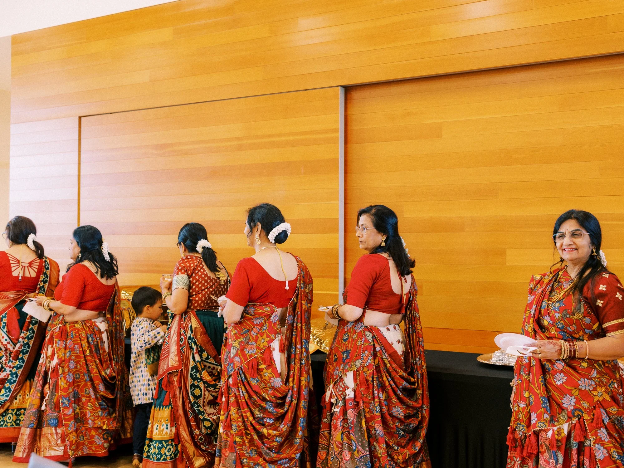 Women in coordinated red patterned traditional outfits gathering together during the Mehndi event.