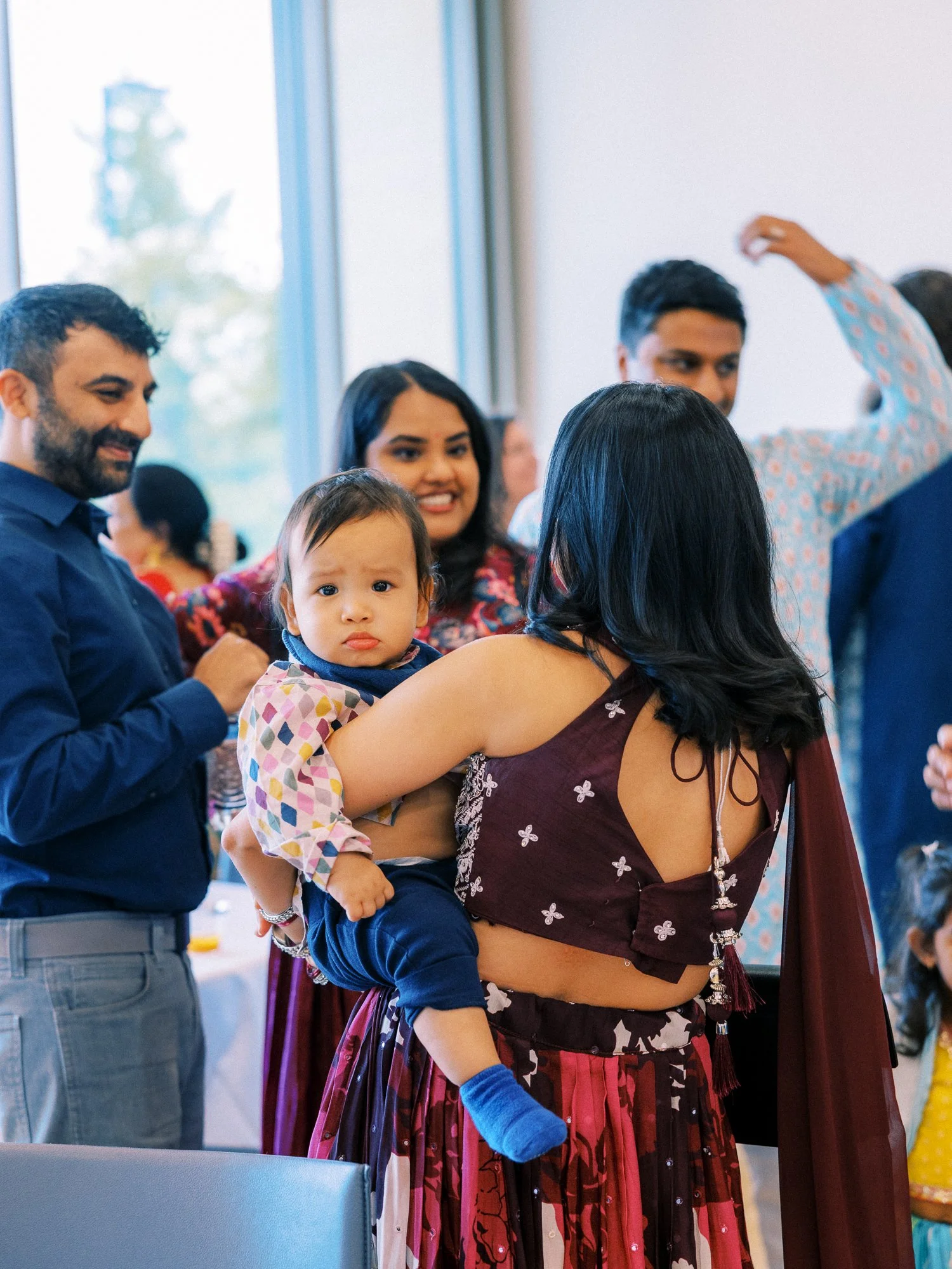 Guest holding a baby while family and friends gather indoors during the Mehndi celebration.
