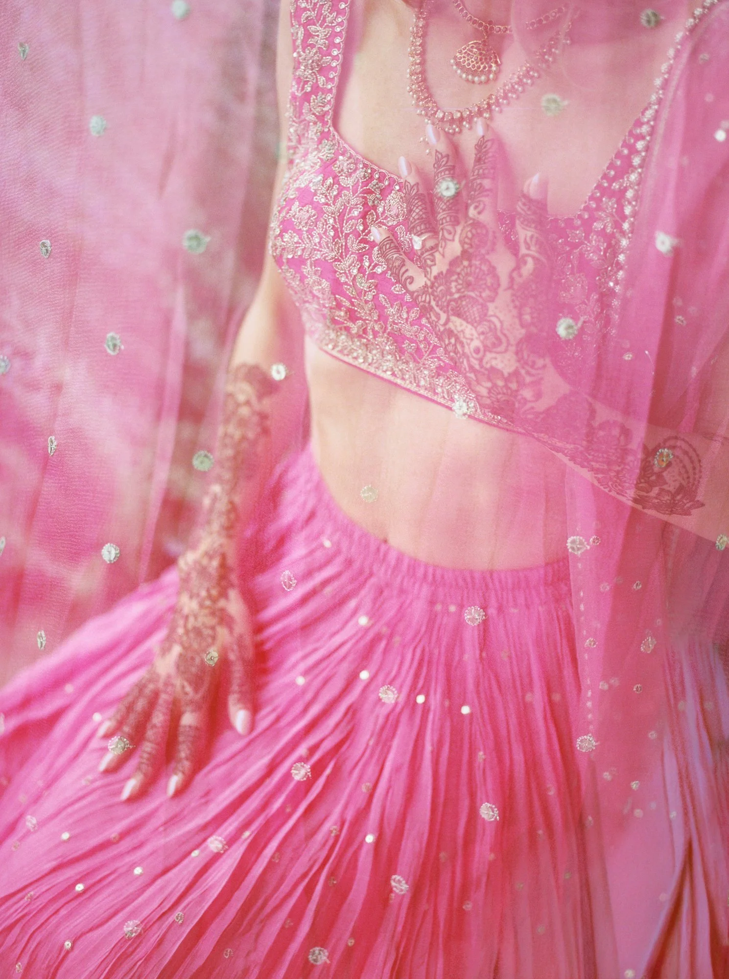 Close-up of Alacia’s pink embroidered outfit and detailed henna-covered hands.