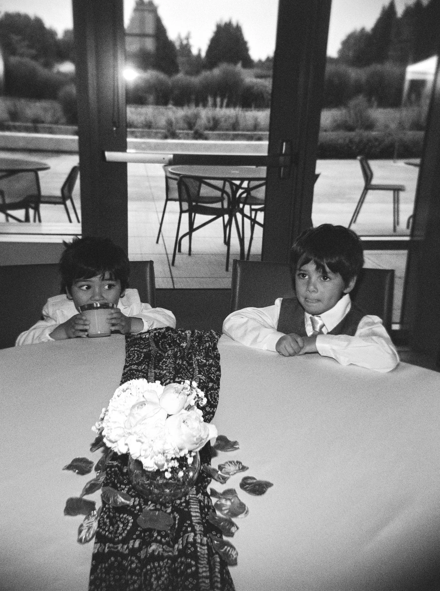 Black-and-white candid of two young boys seated at a table during the Mehndi celebration.