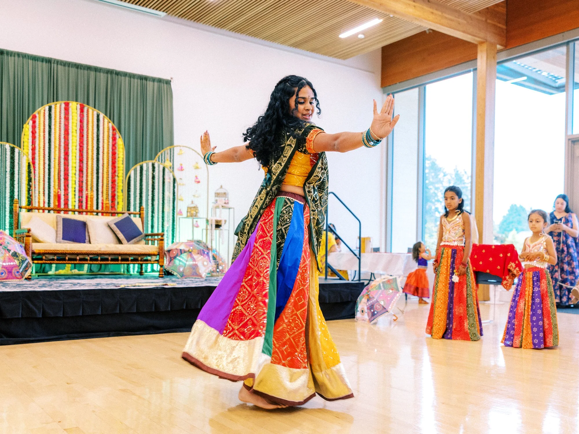 Young dancer in a mirrored top and colorful skirt performs during the Mehndi ceremony.